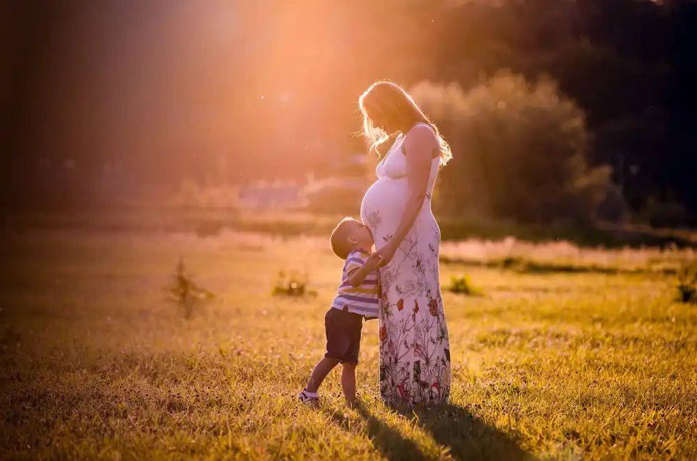 A mother holds her baby over her shoulder, looking out at a green field.