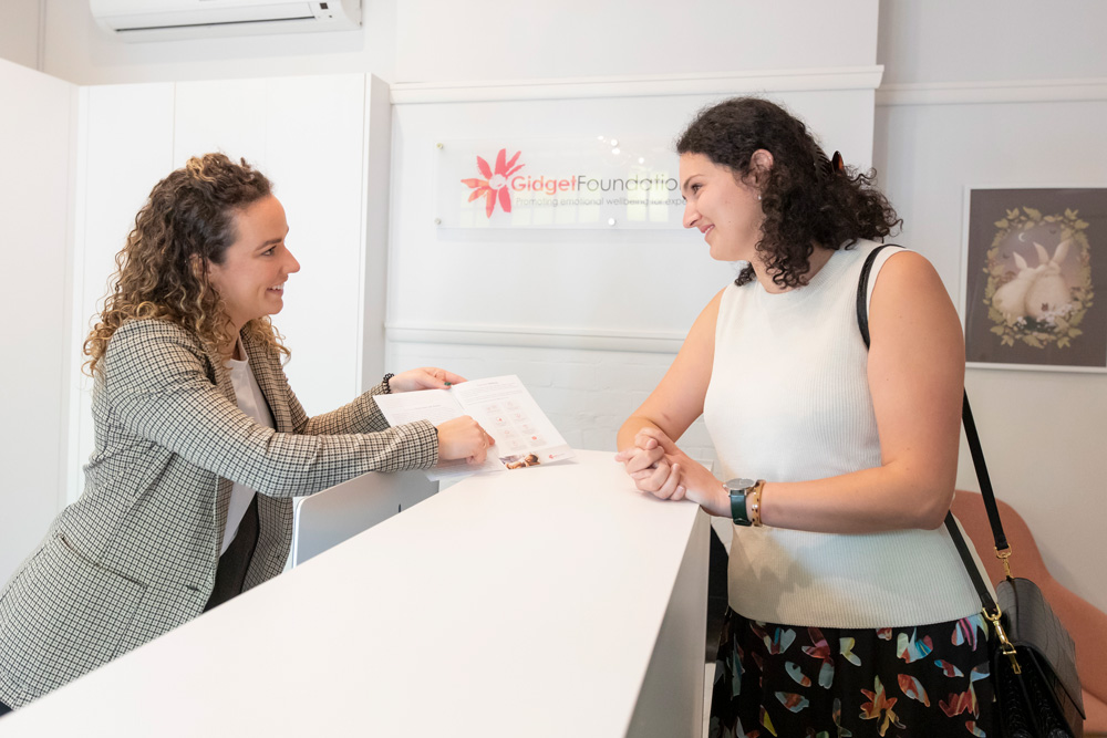 A patient converses with a receptionist at a clinic's reception desk.