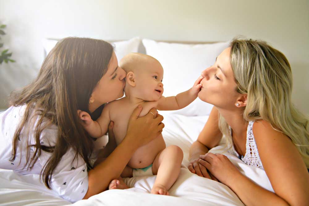 Lesbian family playing on bed with newborn baby