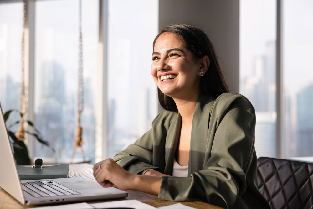 Woman smiles while working on a laptop in a city office