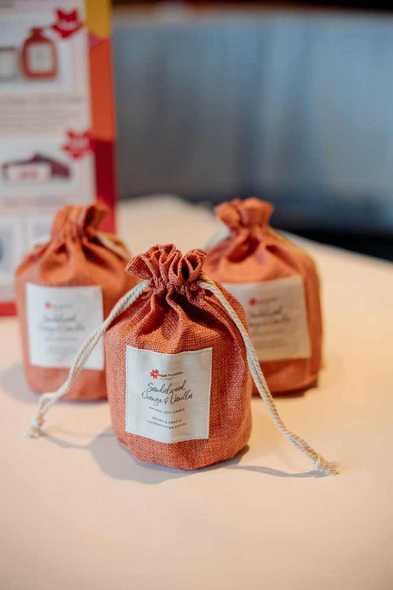 Three orange candles labelled sandalwood, orange, and vanilla on a white surface.