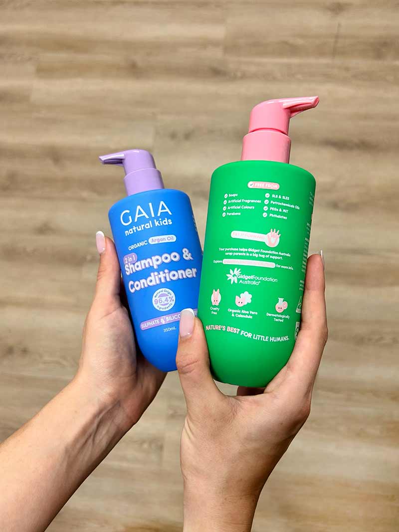 Hands holding Gaia natural kids 2-in-1 shampoo & conditioner and a green lotion bottle with pink pump.