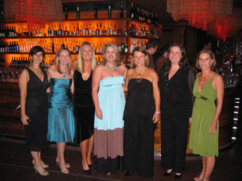 Founders dressed formally standing side by side in front of a bar with illuminated shelves of bottles.