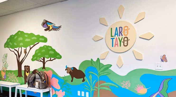 Colorful hand-painted mural at Laro Tayo featuring a sun, trees, birds, and a carabao, with the 'Laro Tayo' logo in the center