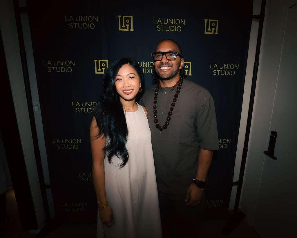 Sonia-Lynn and Sergio Max, founders of La Union Studio, smiling together in front of a step-and-repeat backdrop with the La Union Studio logo