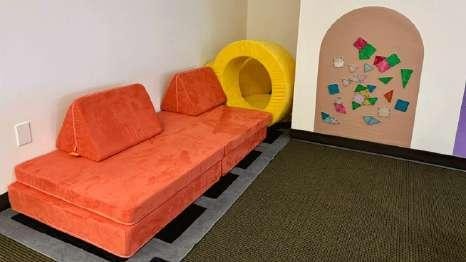 Orange play couch and cushions next to a wall with colorful shape cutouts at Laro Tayo
