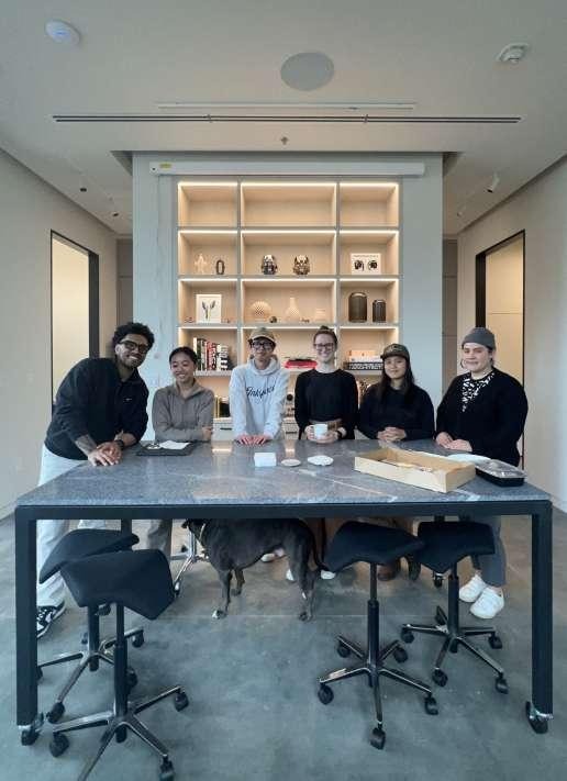 Six team members posing together and smiling around a table at La Union Studio's new headquarters, styled with built-in shelving in the background