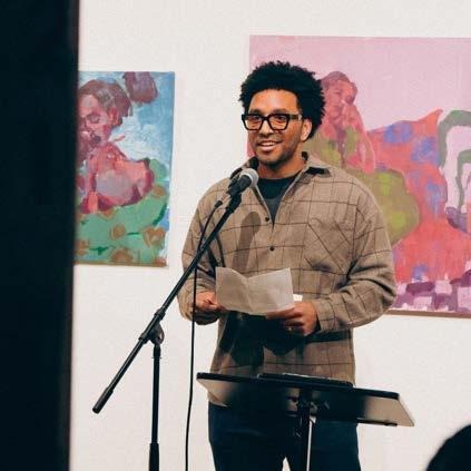 Sergio Legon-Talamoni speaking at a podium with colorful paintings displayed behind him