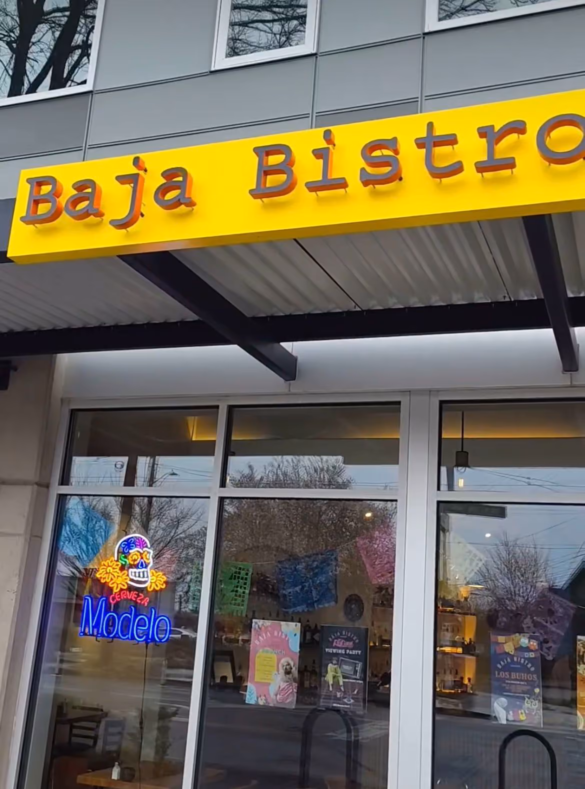 Baja Bistro restaurant storefront with a yellow overhead sign and neon 'Modelo' sign in the window