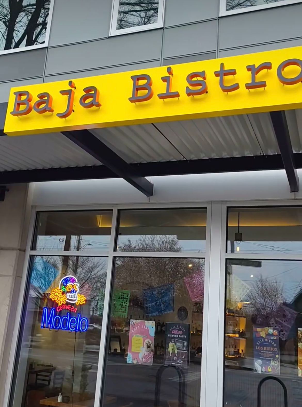Baja Bistro restaurant storefront with a yellow overhead sign and neon 'Modelo' sign in the window