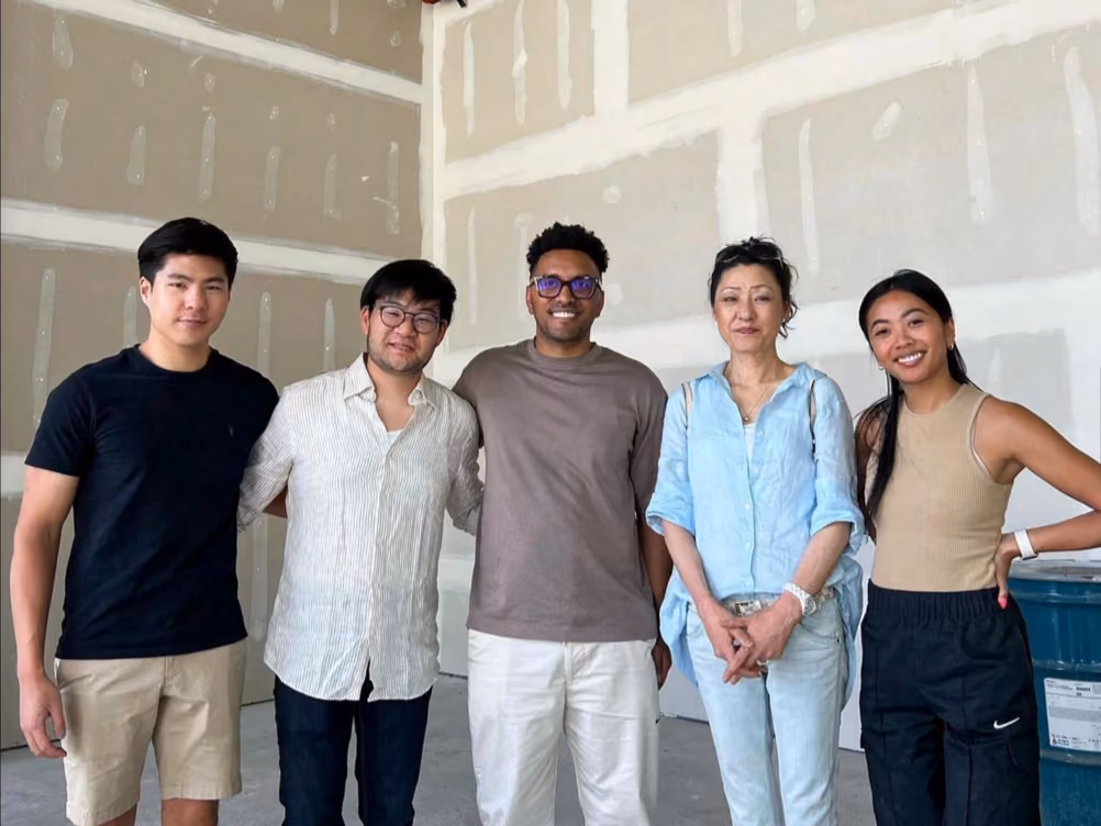 Five people standing together inside an unfinished construction space with exposed drywall