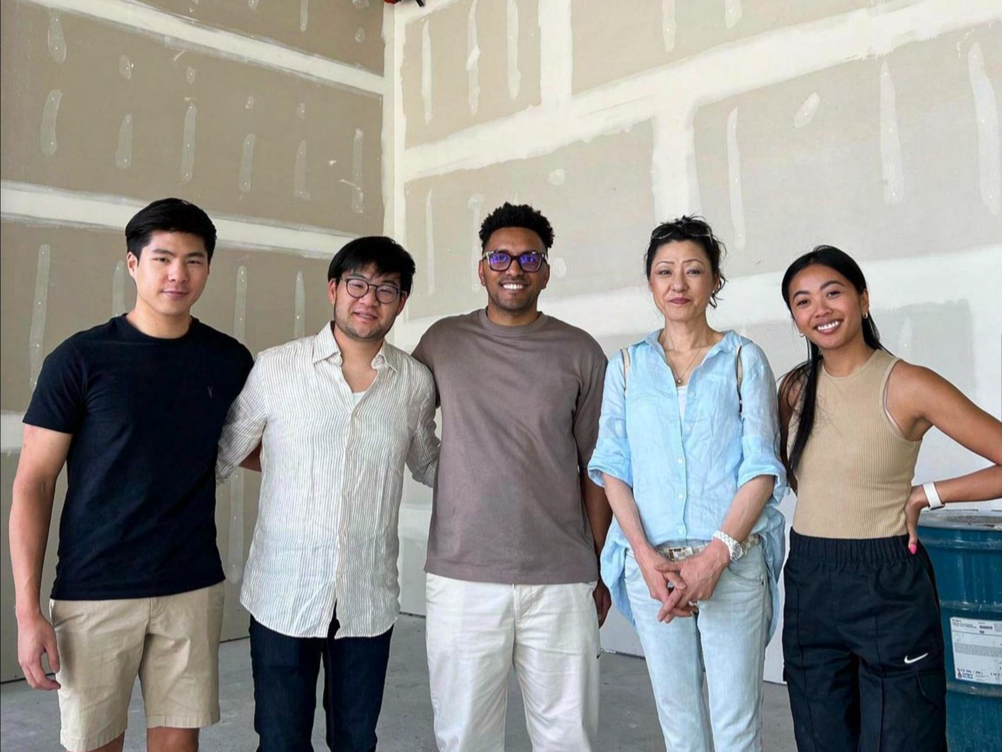 Five people standing together inside an unfinished construction space with exposed drywall