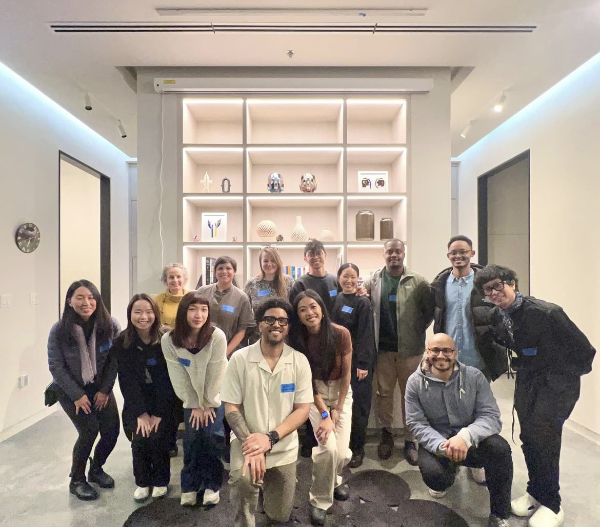 Large group of about fifteen people posing together in a modern office space with built-in display shelving