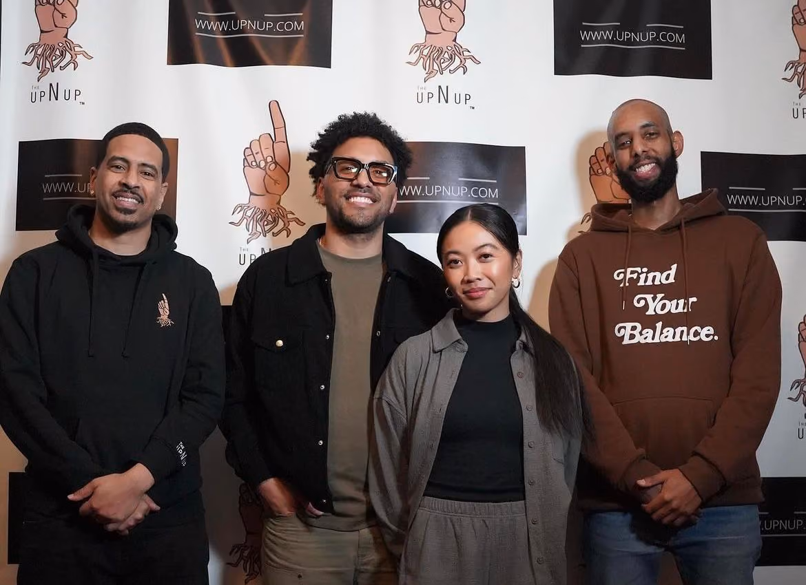 Four people standing together in front of a step-and-repeat banner reading 'UpNUp'