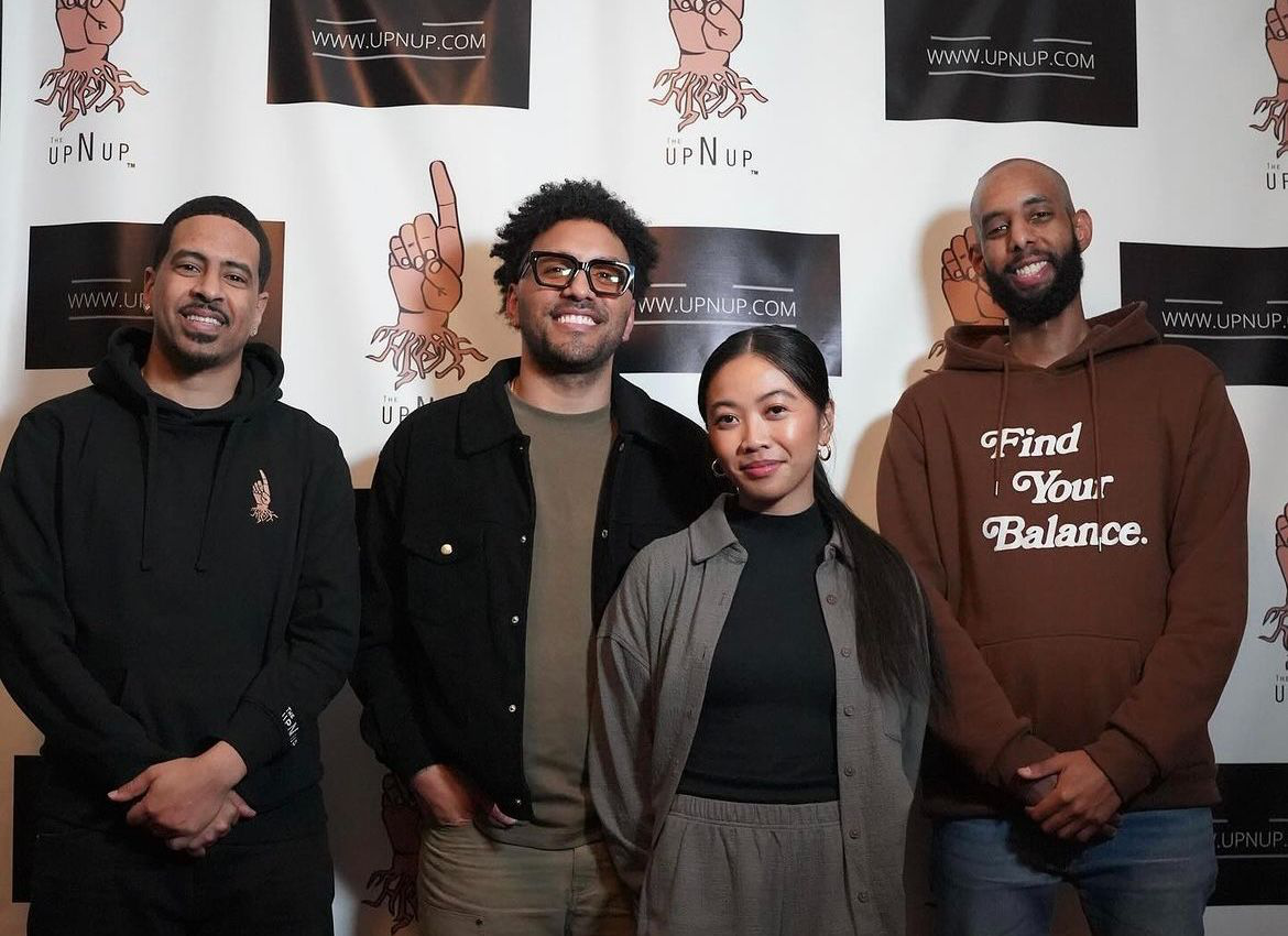 Four people standing together in front of a step-and-repeat banner reading 'UpNUp'