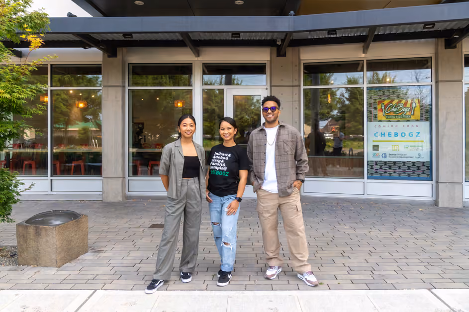 Three people standing outside a storefront with large windows, one wearing a shirt with a logo