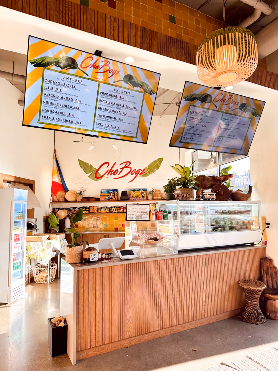 Restaurant counter with two hanging menu screens showing Filipino dishes, a rattan pendant lamp, and a Philippine flag