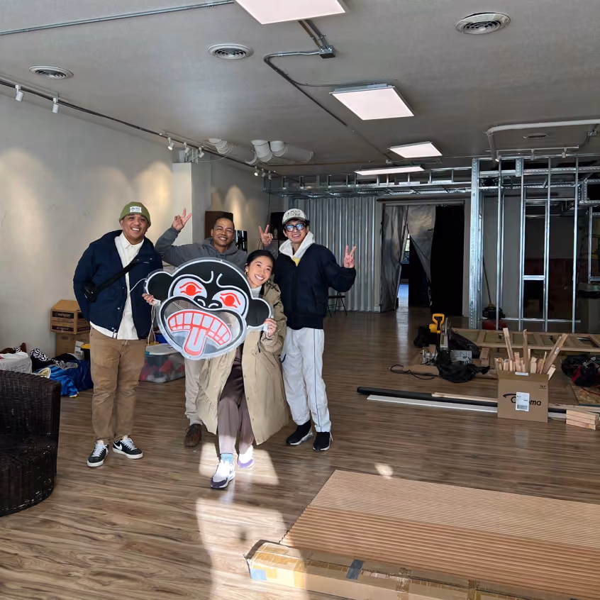 Four people posing playfully in a space under construction, one holding a cartoon mask over their face
