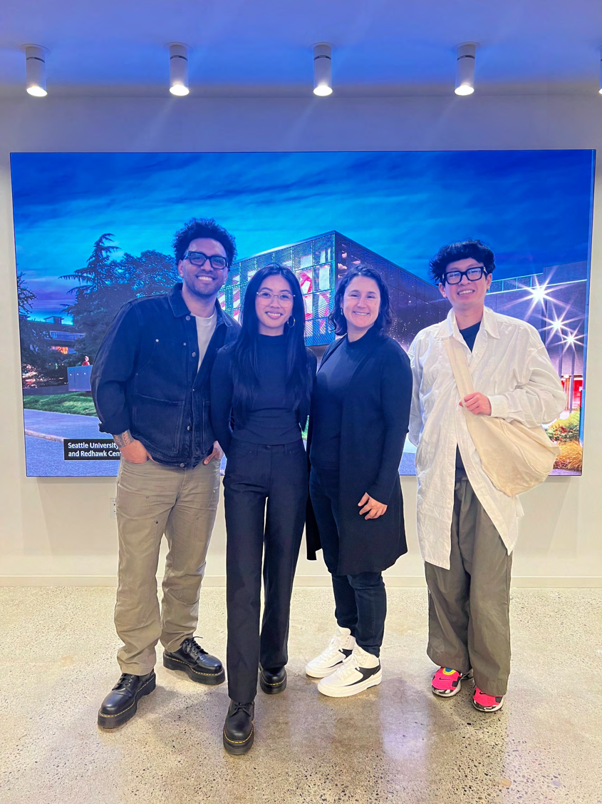 Four people standing together in front of a large photo mural of a building at dusk