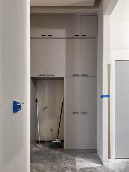 Unfinished interior space with built-in gray cabinetry, a mop and broom leaning against the wall, and painter's tape on an outlet