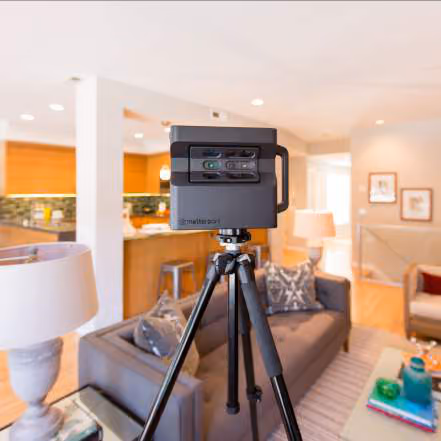 Matterport 3D scanning camera on a tripod set up in a bright living room with a sofa and armchair