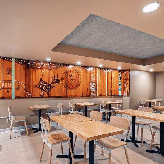 Cafe interior with wood tables and chairs, and a wall mural made of carved wood panels with African-inspired patterns