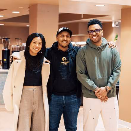 Three people standing together with arms around each other in a cafe, smiling at the camera