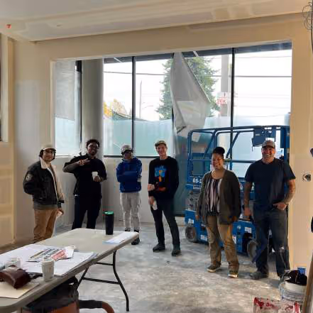 Six people standing together in an unfinished office space with a lift machine and folding table in the foreground
