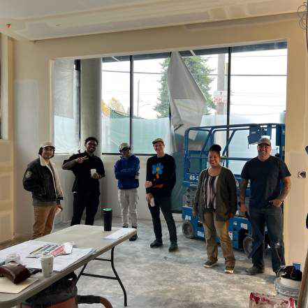 Six people standing together in an unfinished office space with a lift machine and folding table in the foreground