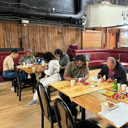 Several people seated at wood tables working on design materials in a restaurant space with red booth seating