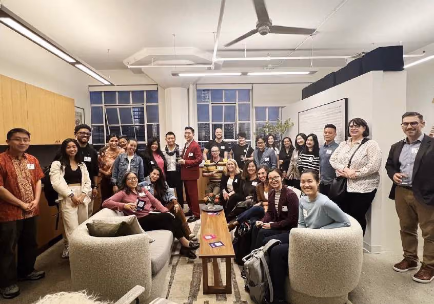 Large group of people gathered in a loft-style office with round armchairs and large windows, posing for a group photo