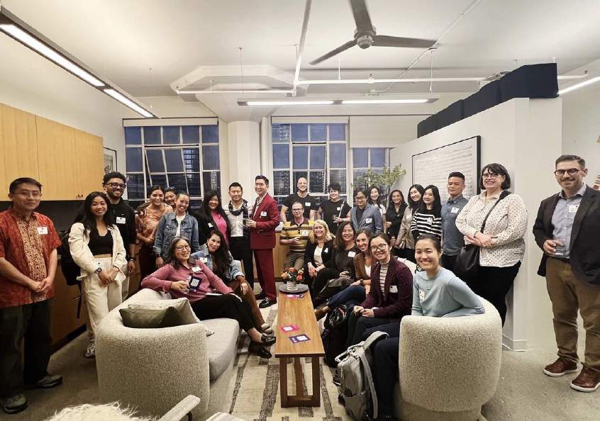 Large group of people gathered in a loft-style office with round armchairs and large windows, posing for a group photo