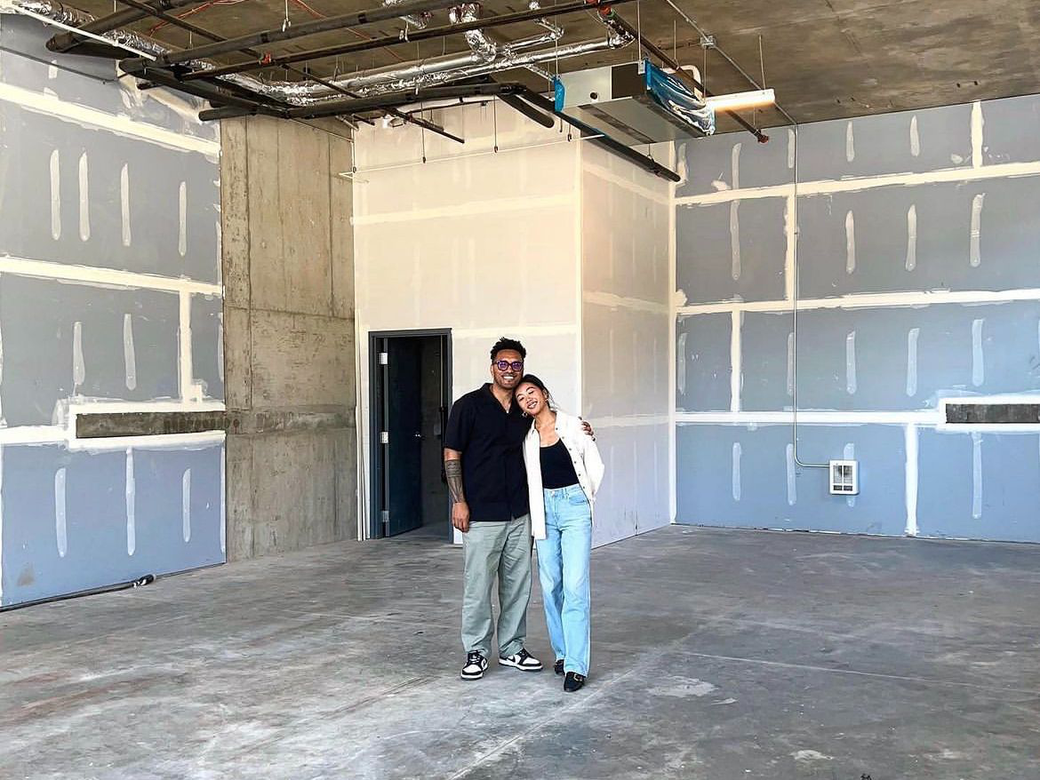 Man and woman standing together in an unfinished office space with exposed drywall and concrete floors