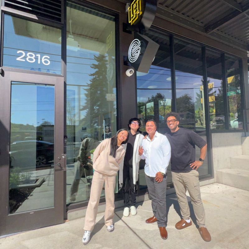 Four members of the La Union Studio team standing together and smiling outside the studio's glass storefront entrance, numbered 2816, on a sunny day.