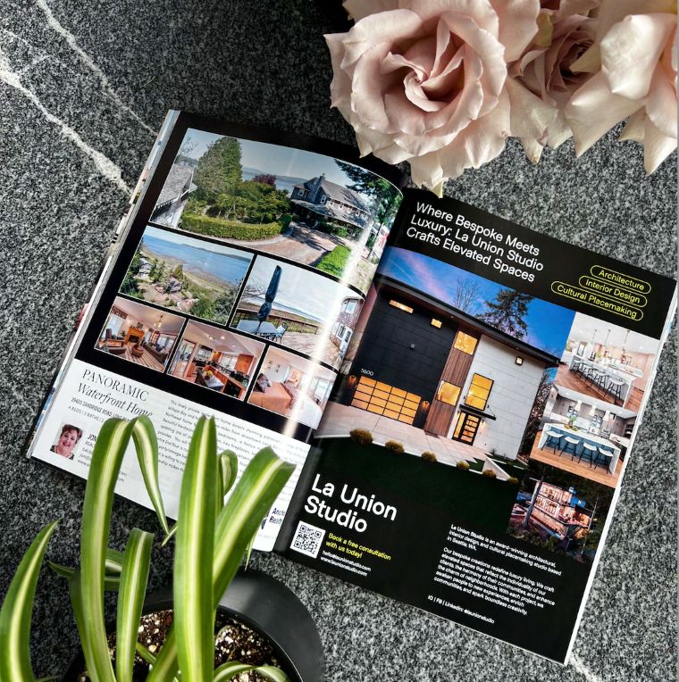 An open copy of HAVEN Lifestyle Magazine resting on a speckled stone surface beside pale roses and a potted plant, showing a two-page feature on La Union Studio with photographs of a waterfront home and interior projects.