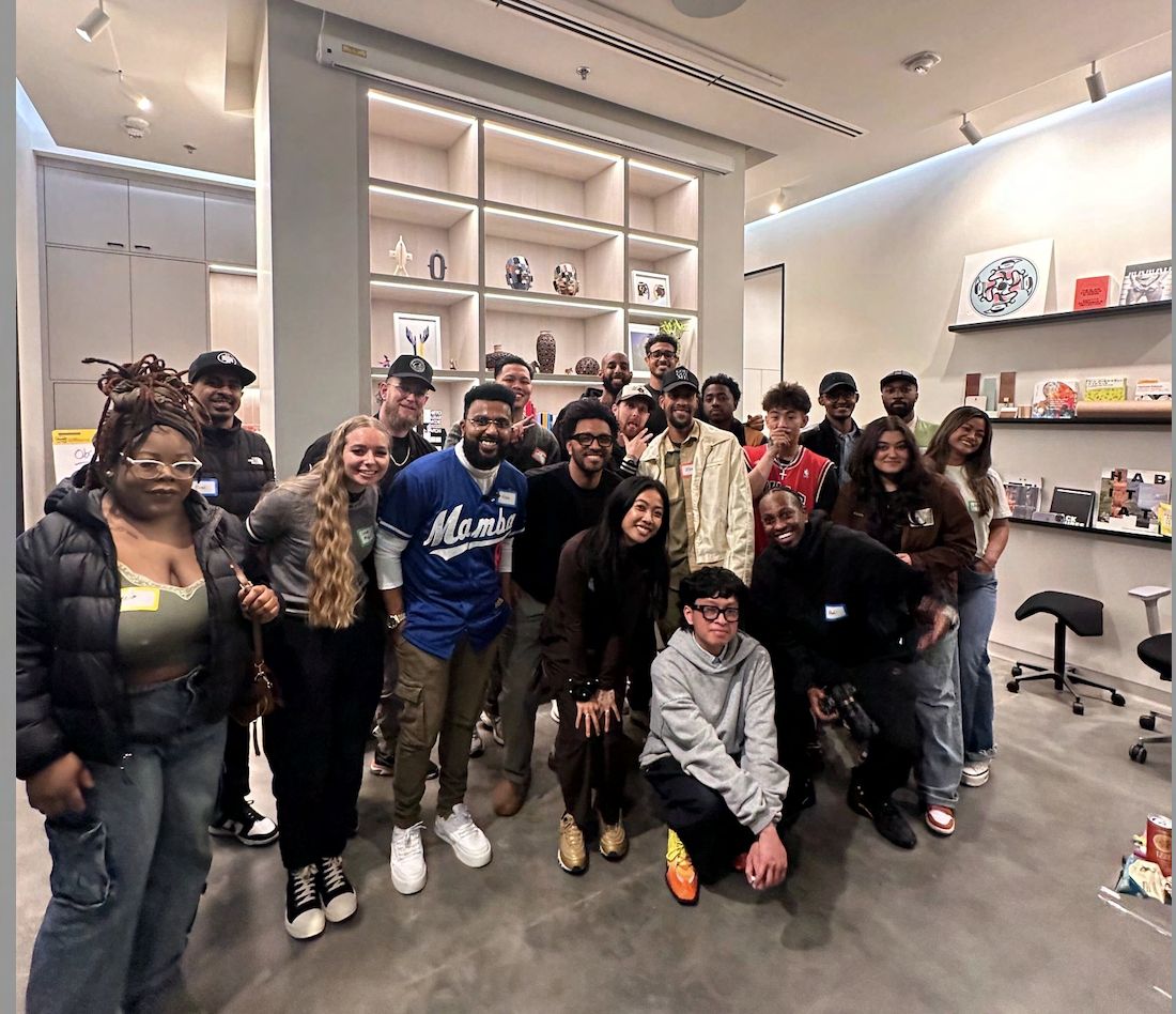 A large group of roughly twenty workshop attendees gathered together for a group photo inside the La Union Studio space, in front of shelves displaying objects and artwork.