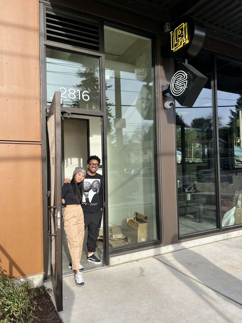 Two people standing together in the open glass doorway of the La Union Studio storefront, numbered 2816, with the studio's logo decals on the windows.