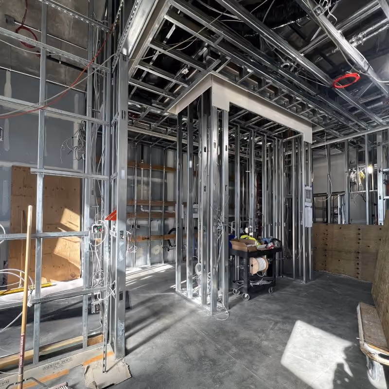 The La Union Studio HQ mid-construction: bare metal stud framing forming interior walls and a doorway, exposed ceiling structure and ductwork above, an unfinished concrete floor, and sunlight falling across the space.