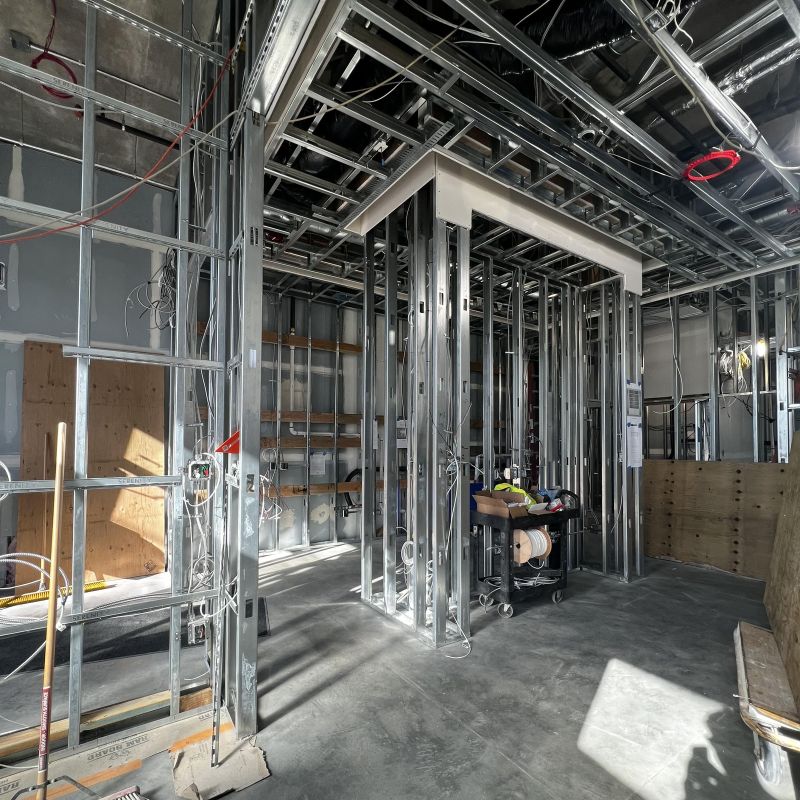 The La Union Studio HQ mid-construction: bare metal stud framing forming interior walls and a doorway, exposed ceiling structure and ductwork above, an unfinished concrete floor, and sunlight falling across the space.