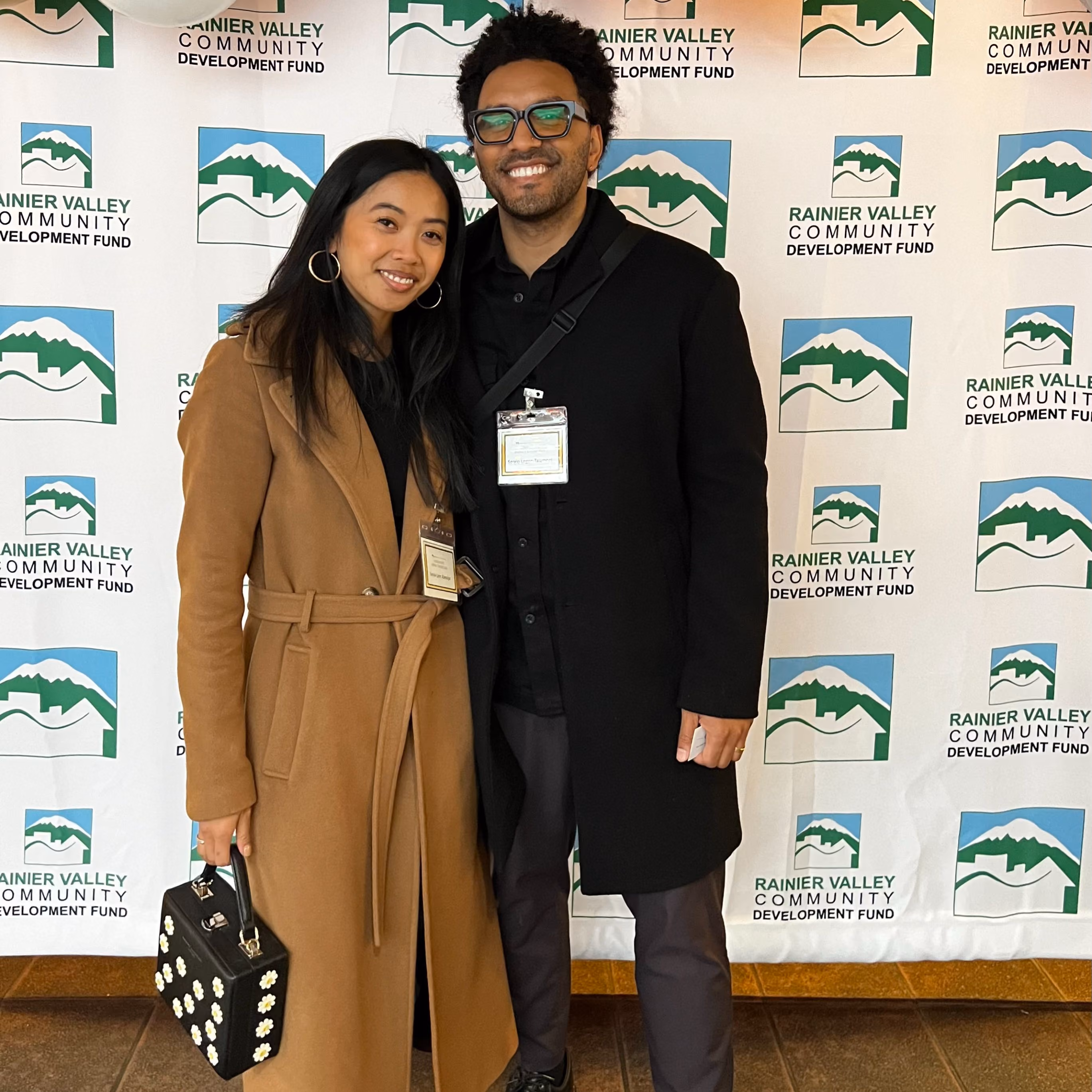 Two people posing side by side in front of a step-and-repeat banner printed with the Rainier Valley Community Development Fund logo.