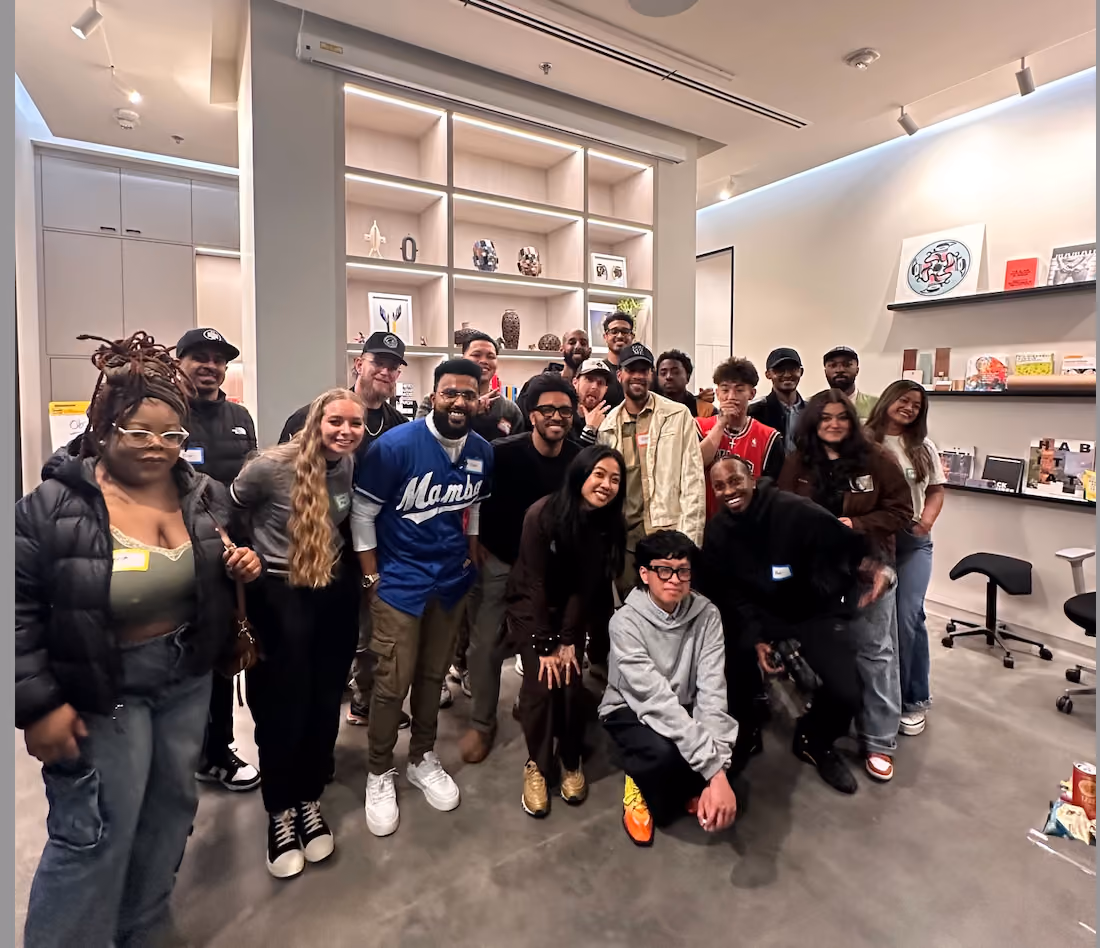 A large group of roughly twenty workshop attendees gathered together for a group photo inside the La Union Studio space, in front of shelves displaying objects and artwork.