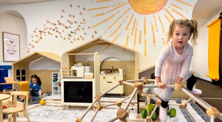 Young child climbing a wooden play structure inside Laro Tayo's brightly decorated indoor play space, with another child playing nearby
