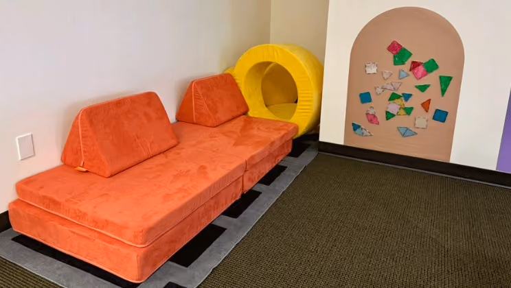 Orange play couch and cushions next to a wall with colorful shape cutouts at Laro Tayo