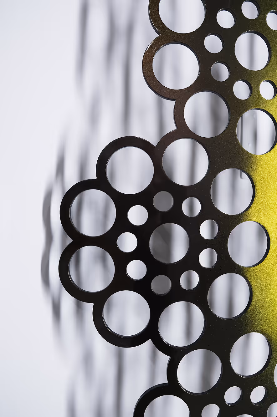 Sort metalplade med cirkulære udskæringer og skygger mod en hvid baggrund.
