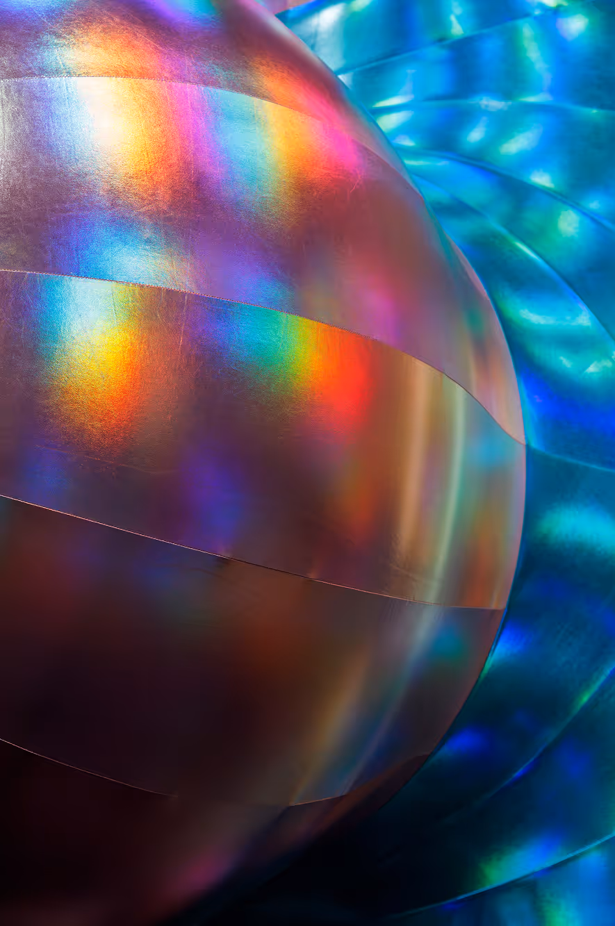 Nærbillede af et reflekterende, metallisk kugle med regnbuefarvede lysreflektioner.