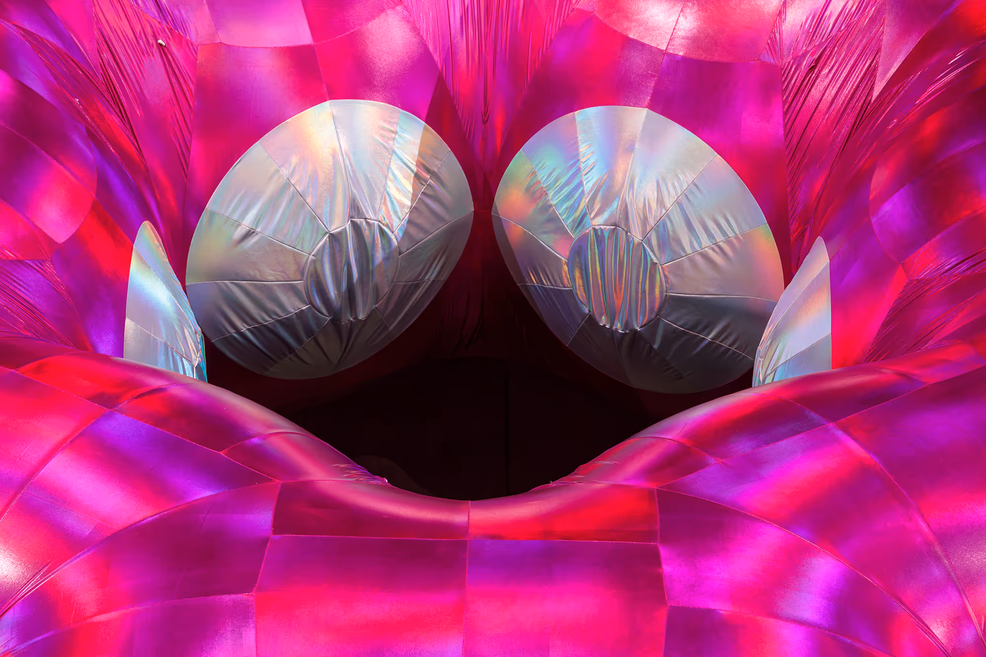 Nærbillede af en farverig, oppustelig struktur med to store, sølvfarvede cirkulære former og levende pink-røde nuancer.