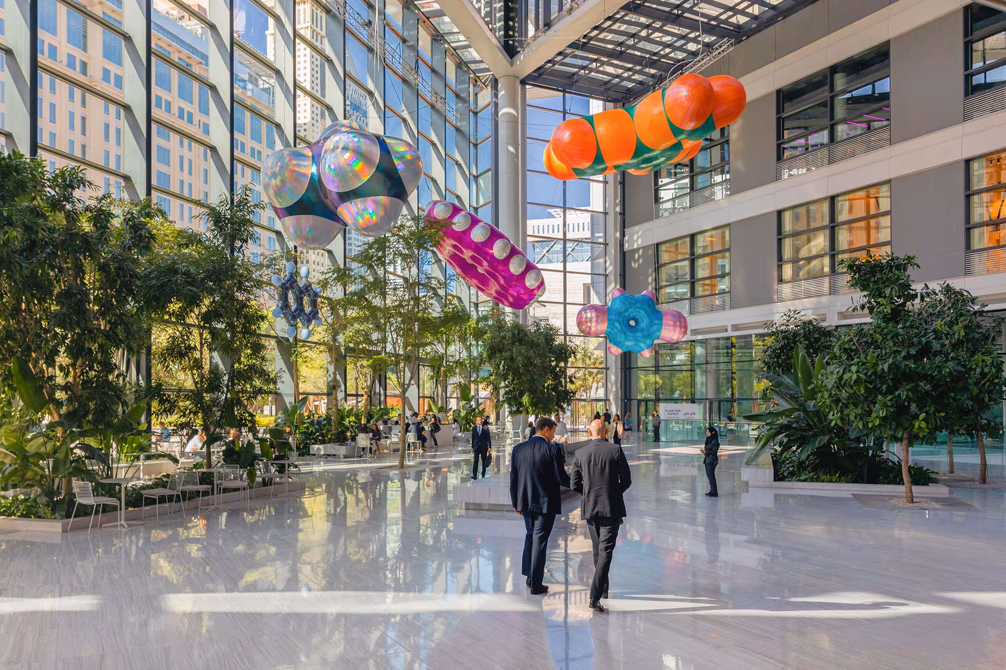 Moderne kontorbygning med glasvægge, store grønne planter og farverige, oppustede kunstinstallationer hængende fra loftet.