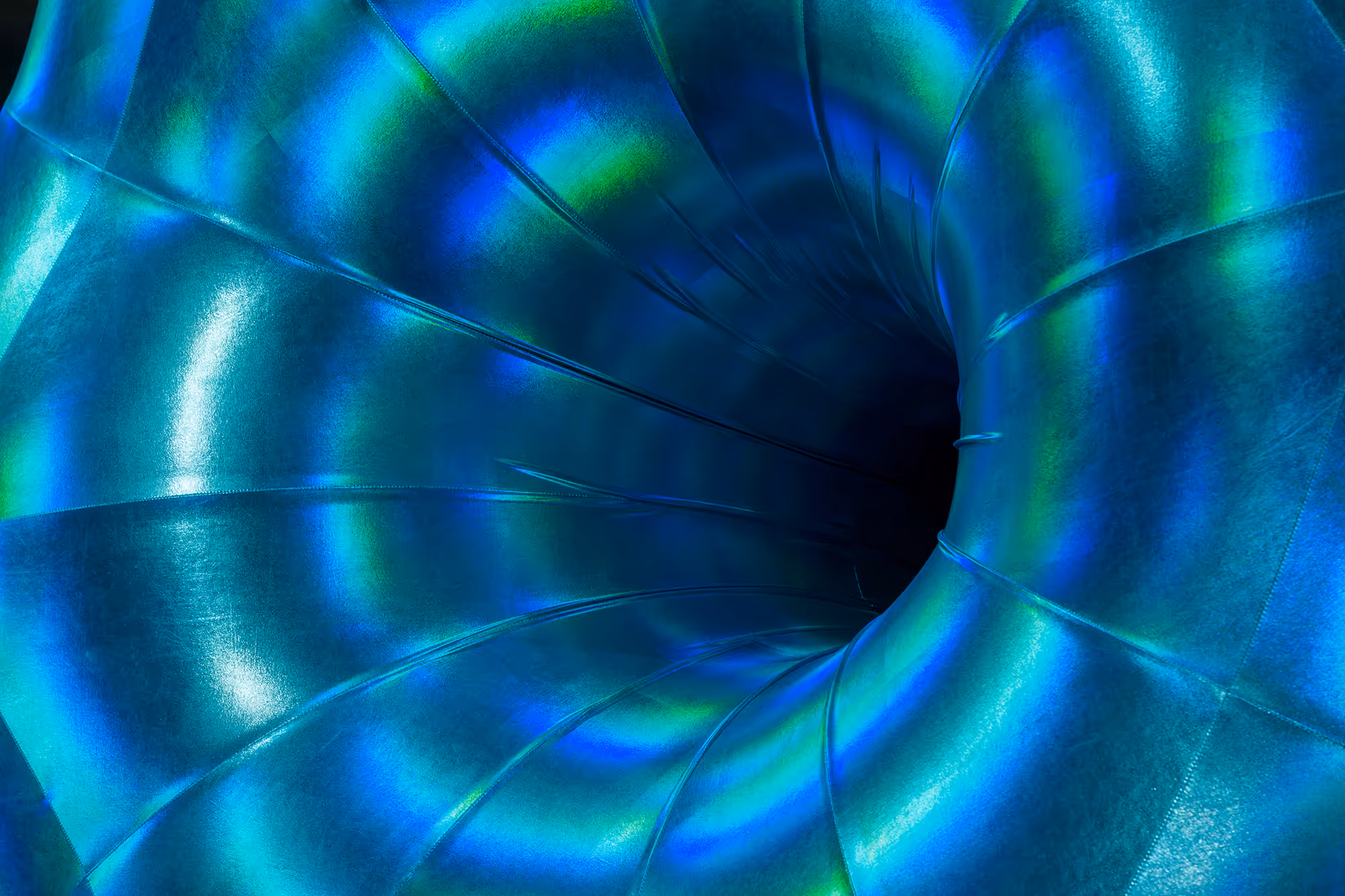 Nærbillede af en blågrøn, spiralformet metalrør med skinnende overflade og mørk midte.