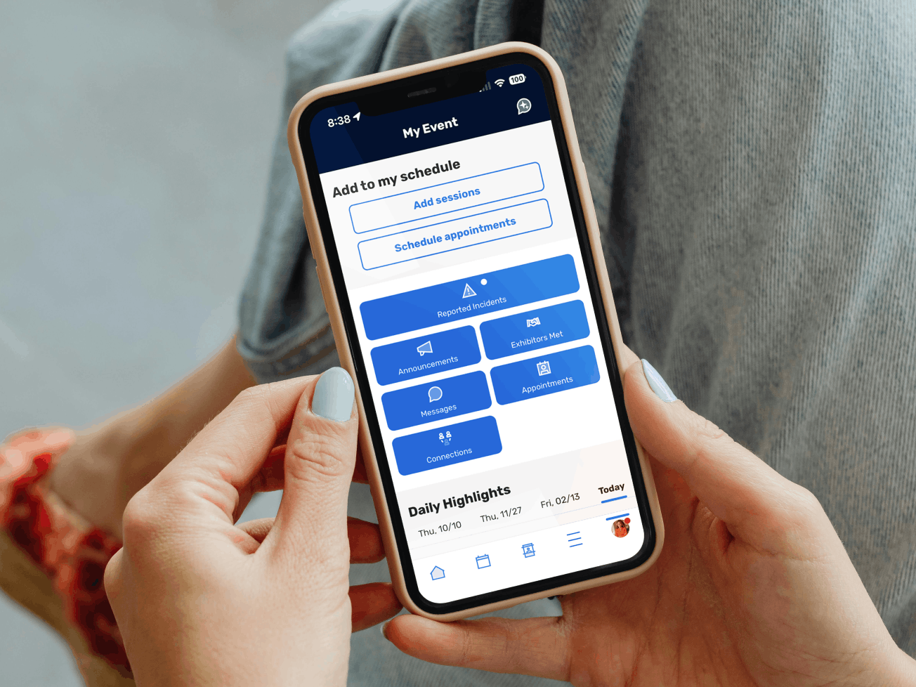 A person holding a smartphone displaying the Attendee Hub mobile app's event dashboard, showing options for announcements, messages, appointments, and daily highlights