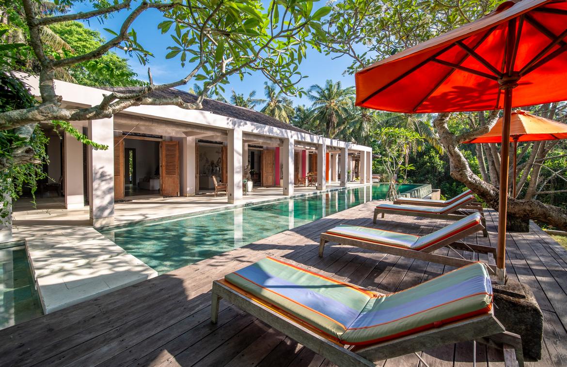 Set on a sprawling 4,000 sqm terraced landscape that cascades down to a majestic river, this architectural masterpiece is a standout creation. Designed by the late renowned Terry Brooks, as his private residence,every element reflects the heart and vison of this amazing designer.‍Nestled in the tranquil village of Nyambu, this property is surrounded by nature yet enjoys convenient access to Bali's hotspots—just a short drive to Canggu in the south and less than an hour to Ubud in the north.‍The estate comprises four distinct buildings:‍1. The Main ResidenceA blend of modern colonial charm and elegant design, the main building boasts high-pitched wooden ceilings that create an airy, grand ambiance. Antique double teak doors and a covered patio running the length of the building add timeless character.Central Lounge: A cozy lounge anchors the space, flanked by a 10-seater dining area on one side and a TV lounge on the other.Patio Dining: Two round dining tables on the patio offer an al fresco dining experience with views of the pool and jungle beyond.Swimming Pool & Deck: The expansive 18m infinity pool is complemented by a large wooden deck outfitted with daybeds, perfect for sunbathing or relaxing in the serene surroundings‍‍2. The Master Bedroom PavilionThis private retreat includes a spacious terrace, a built-in wardrobe, and a luxurious semi-open bathroom. Adjacent to the suite is a dedicated spa room complete with a massage table and a terrazzo bathtub, offering a truly indulgent experience.‍3. Lower Level Waterfall PavilionThe estate's lower level houses a two-bedroom pavilion with en-suite bathrooms and serene views of lush greenery. ‍4. The Garden PavilionInspired by traditional Javanese Joglo architecture, this open-plan structure sits near the entry to the property and features three en-suite bedrooms, each spaciously designed and complemented by semi-open bathrooms. At the heart of the pavilion lies an inviting open living area, seamlessly connecting to lush gardens framed by coconut trees.‍At the bottom of the property, a stunning natural landscape meets the riverbank. An artificial waterfall cascades from the edge of the pool into a pond below, creating a tranquil focal point. This area also offers untapped potential for additional bedrooms or an entertainment space.‍This exceptional estate is ideal as a luxurious residence, a commercial villa rental, or a private venue, offering an unmatched combination of seclusion, style, and proximity to Bali’s vibrant destinations.